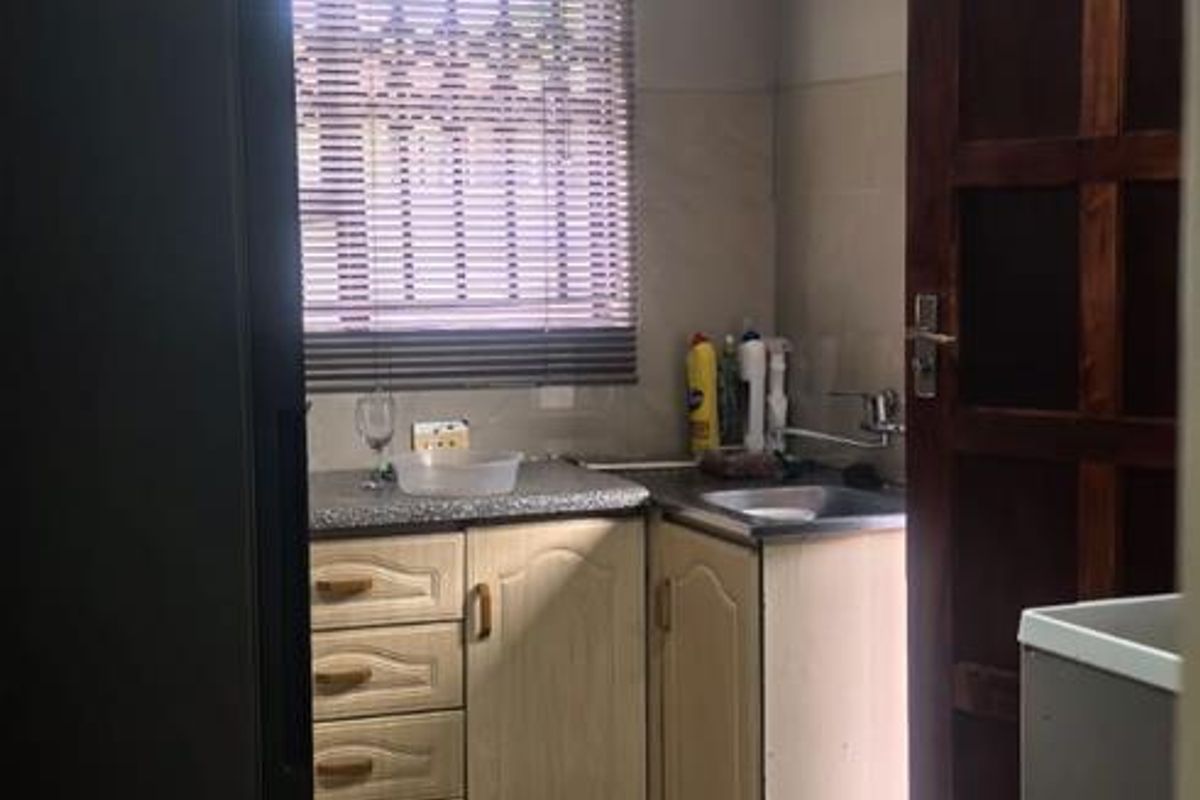 A functional kitchen area featuring tiled flooring, built-in cabinetry, a stainless steel sink, and a window with fitted blinds.
