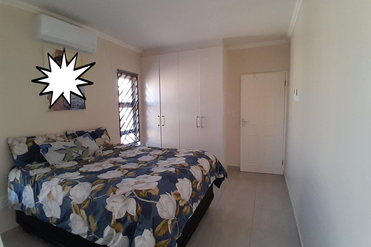 A well-maintained bedroom featuring built-in cupboards, tiled flooring, and a wall-mounted air conditioning unit.