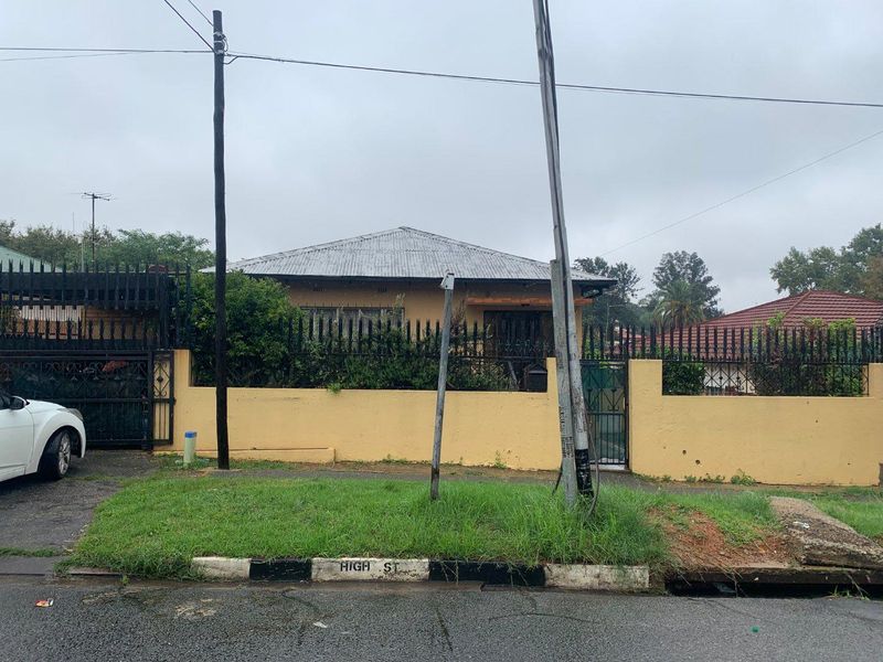 Front view of a single-story house featuring a corrugated metal roof, perimeter wall with metal fencing, and a gated entrance from the street.