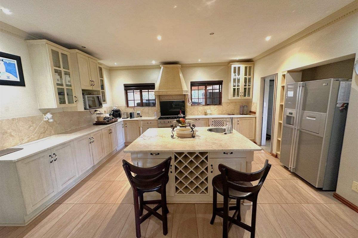Spacious kitchen featuring light-toned cabinetry, a central island with integrated wine rack and prep sink, stone countertops, and recessed ceiling lighting.