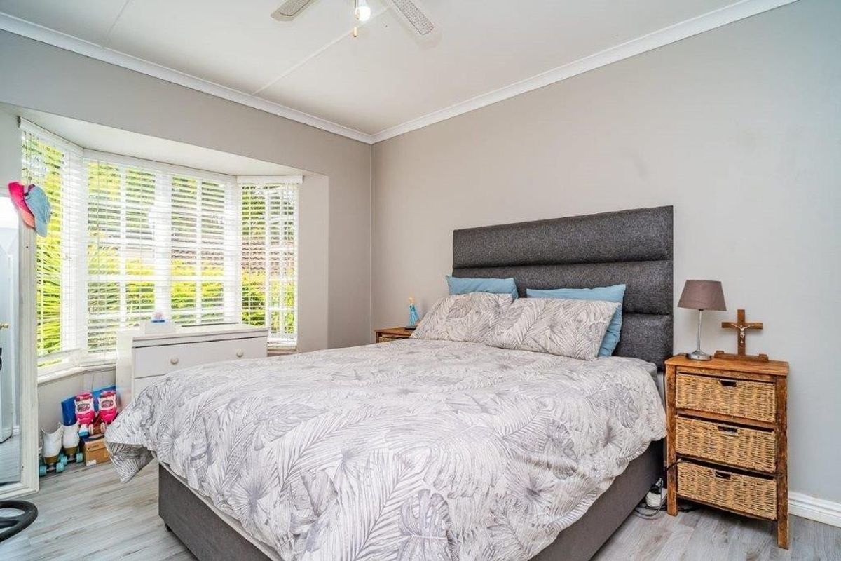 A well-lit bedroom featuring a large bay window, ceiling fan, and modern laminate flooring, providing a comfortable and bright living space.