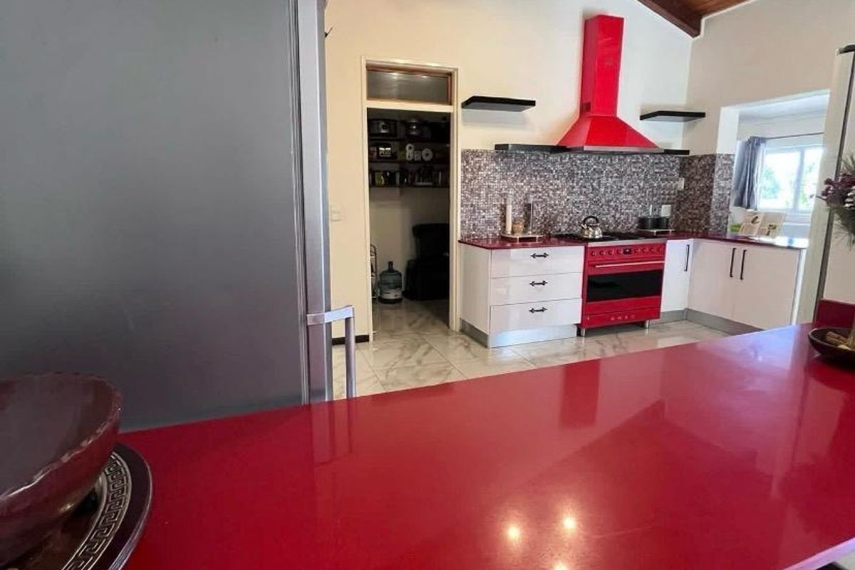 A vibrant kitchen featuring a striking red breakfast bar, matching range cooker and extractor, mosaic splashbacks, and a high exposed timber beam ceiling.