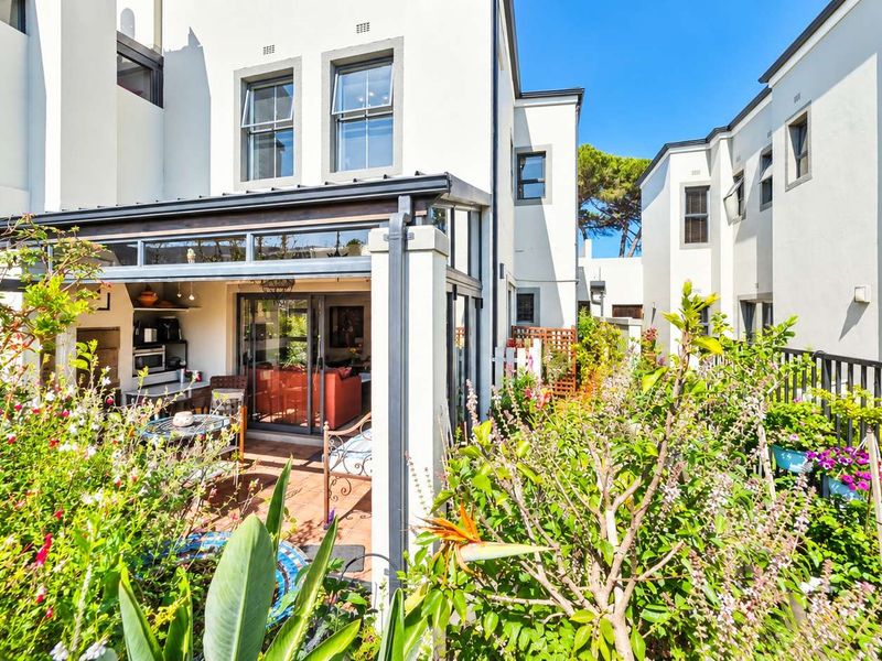 A well-maintained rear townhouse exterior featuring a covered patio area, sliding glass doors, and a lush landscaped garden.