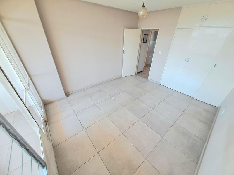 An empty bedroom featuring neutral tiled flooring, built-in cupboards, and a sliding glass door providing access to an outdoor area.