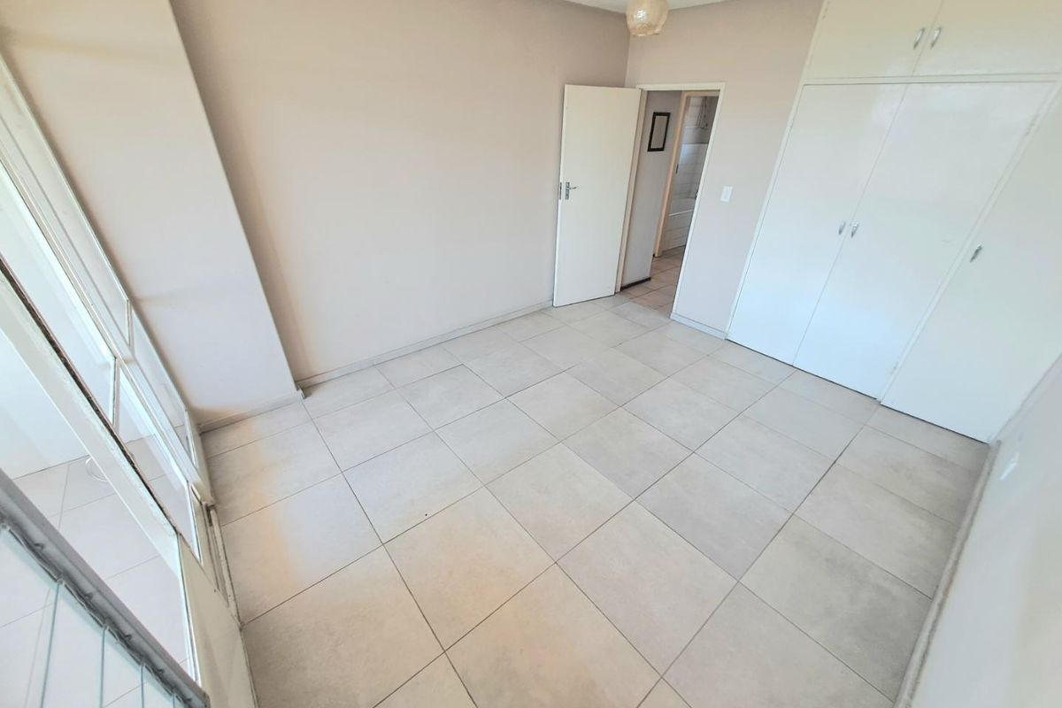 An empty bedroom featuring neutral tiled flooring, built-in cupboards, and a sliding glass door providing access to an outdoor area.
