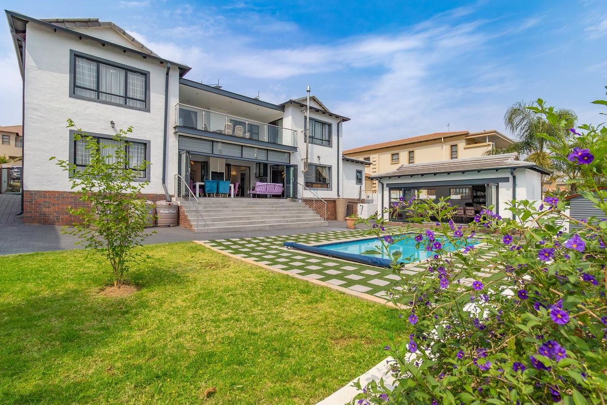 Rear view of the property featuring a landscaped garden, swimming pool, paved patio area, and a detached outbuilding with bi-fold doors.