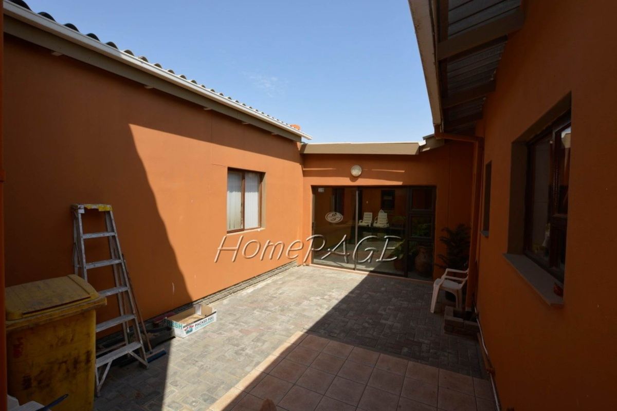 A paved rear courtyard area featuring terracotta-colored exterior walls, sliding glass doors, and tiled flooring, providing a functional outdoor space.