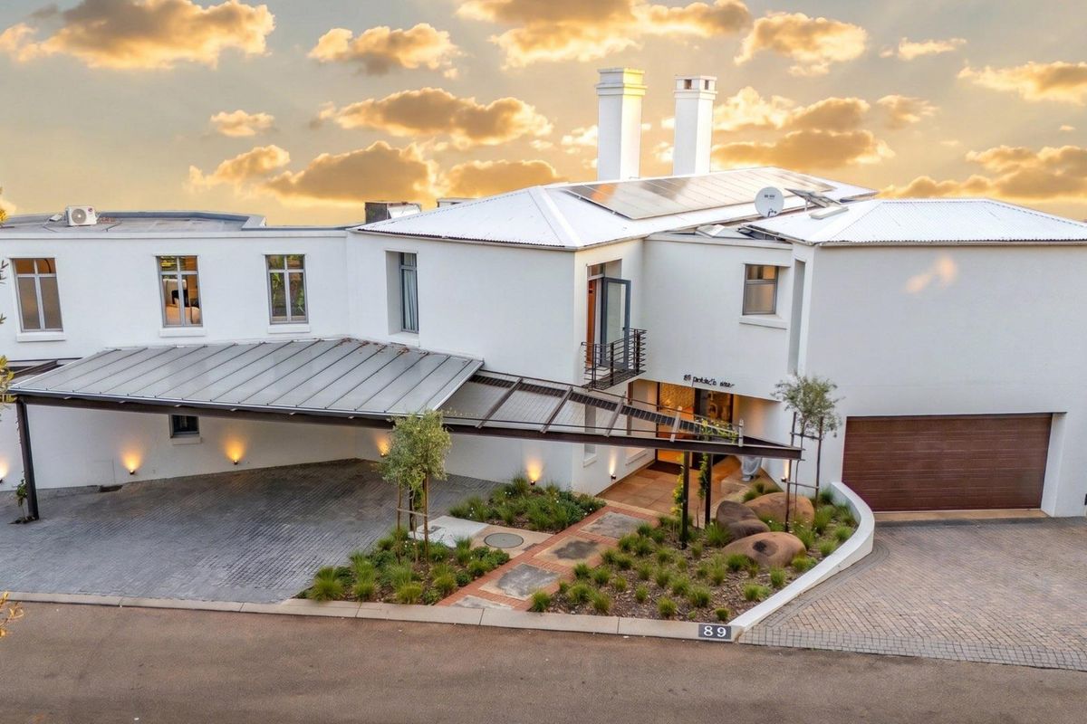 Aerial view of a modern residential property featuring a paved driveway, covered carport, landscaped garden, and solar panels on the roof.