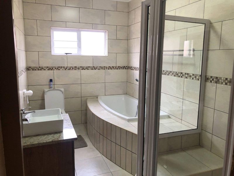 A clean, functional bathroom featuring a built-in bathtub, separate shower enclosure, vanity with granite countertop, and neutral wall tiling.