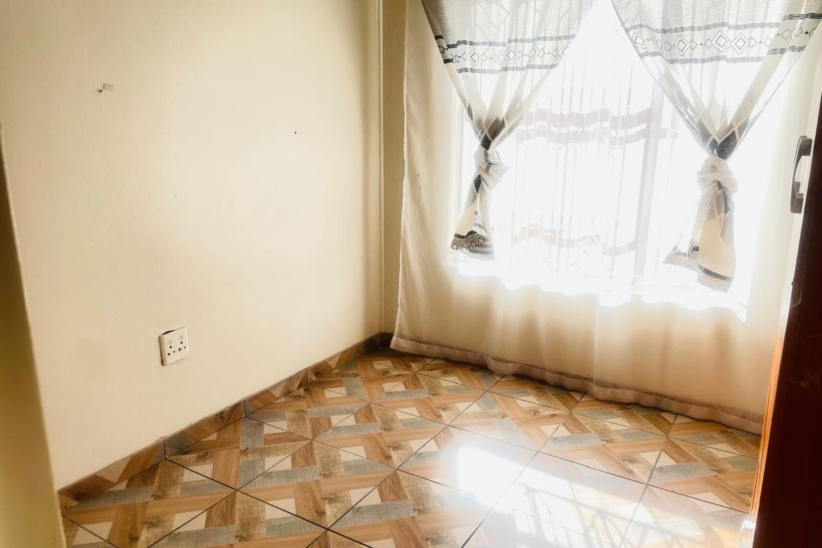 A compact room featuring patterned ceramic floor tiles and a large window allowing natural light, suitable for a small bedroom or home office.