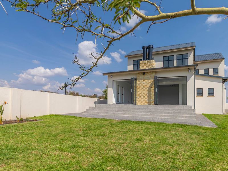 Rear view of a modern double-story house featuring a stone-clad chimney, concrete patio steps, and bi-fold doors leading to a landscaped garden.