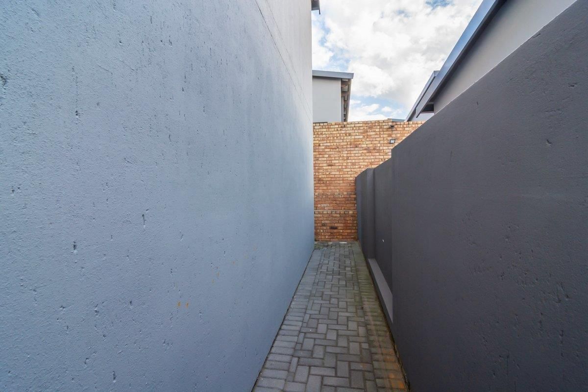 A narrow side passage featuring paved flooring enclosed by painted boundary walls and a brick rear wall.
