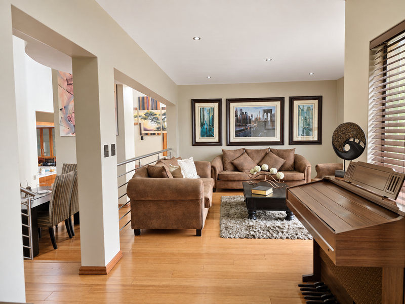 Spacious open-plan living area featuring warm timber flooring, recessed downlighting, and a modern stainless steel balustrade overlooking the adjacent dining space.