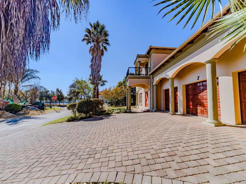 A well-maintained front exterior view featuring a paved driveway, triple garage doors, and an elegant arched portico with balcony above.