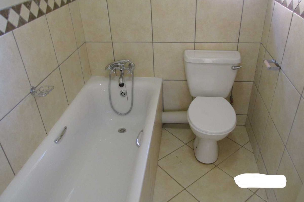 A functional bathroom featuring a standard bathtub, toilet, and neutral ceramic tiling throughout the walls and floor.