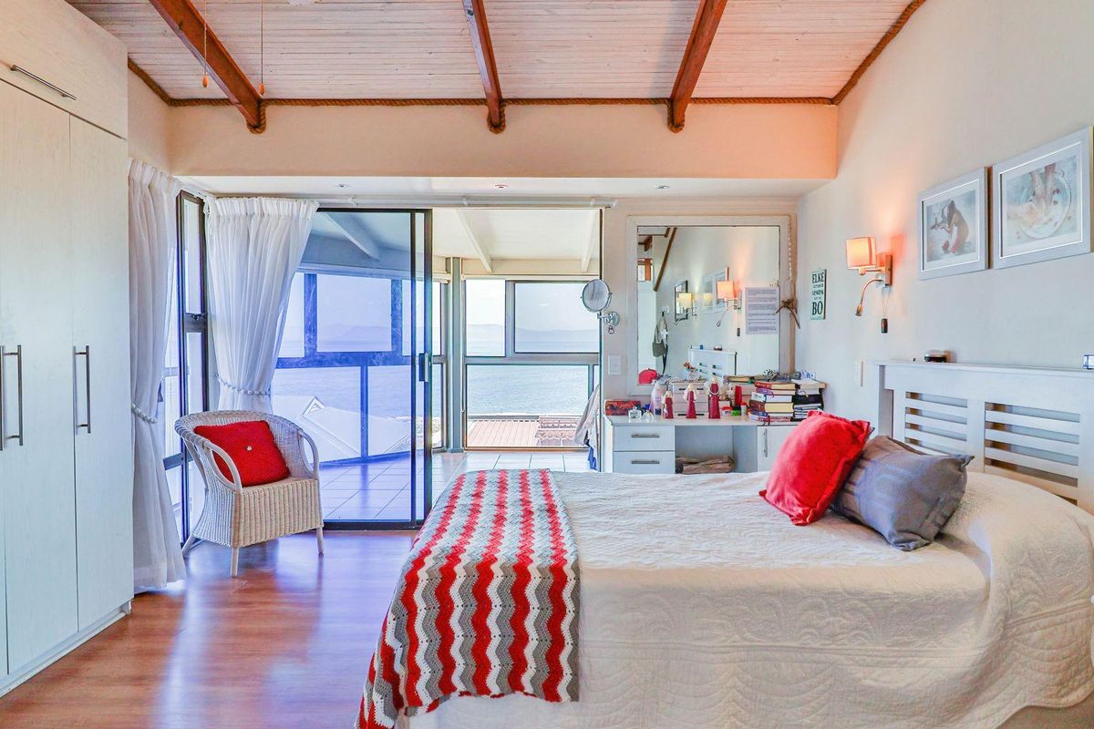 Spacious bedroom featuring exposed timber ceiling beams, built-in wardrobes, and large sliding glass doors opening to a balcony with scenic water views.