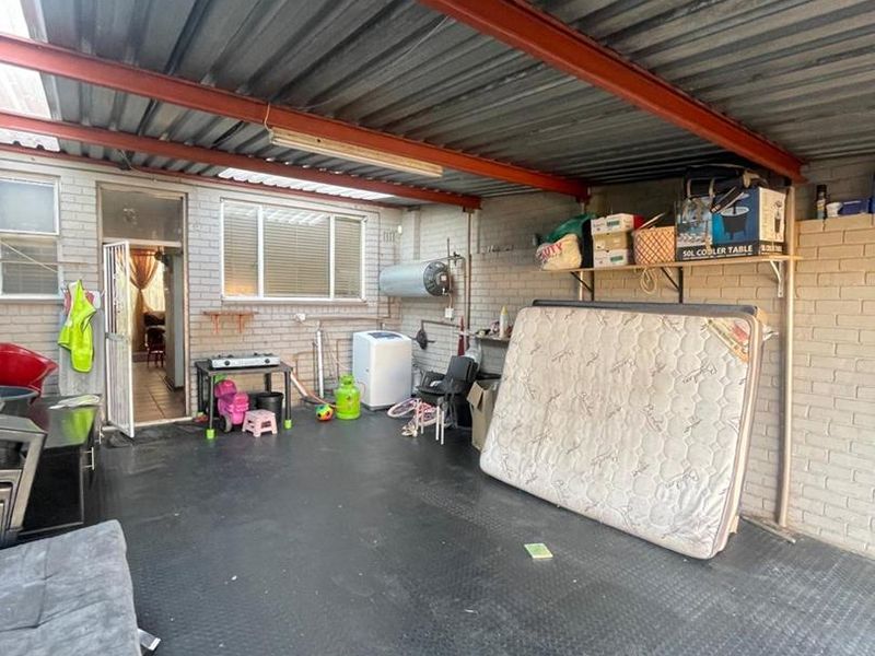A covered outdoor patio area featuring exposed steel beams, brick walls, and durable rubber flooring, suitable for use as a utility or entertainment space.