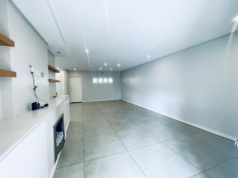 Spacious, empty living area featuring large format floor tiles, recessed downlights, a built-in fireplace, and modern floating shelving.