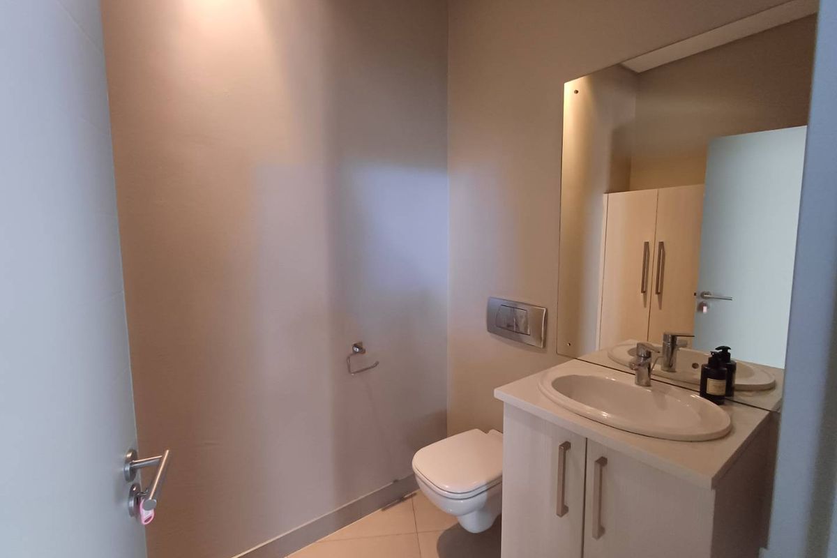 A modern guest bathroom featuring a wall-mounted toilet, a vanity with an integrated basin, and a large wall-mounted mirror.