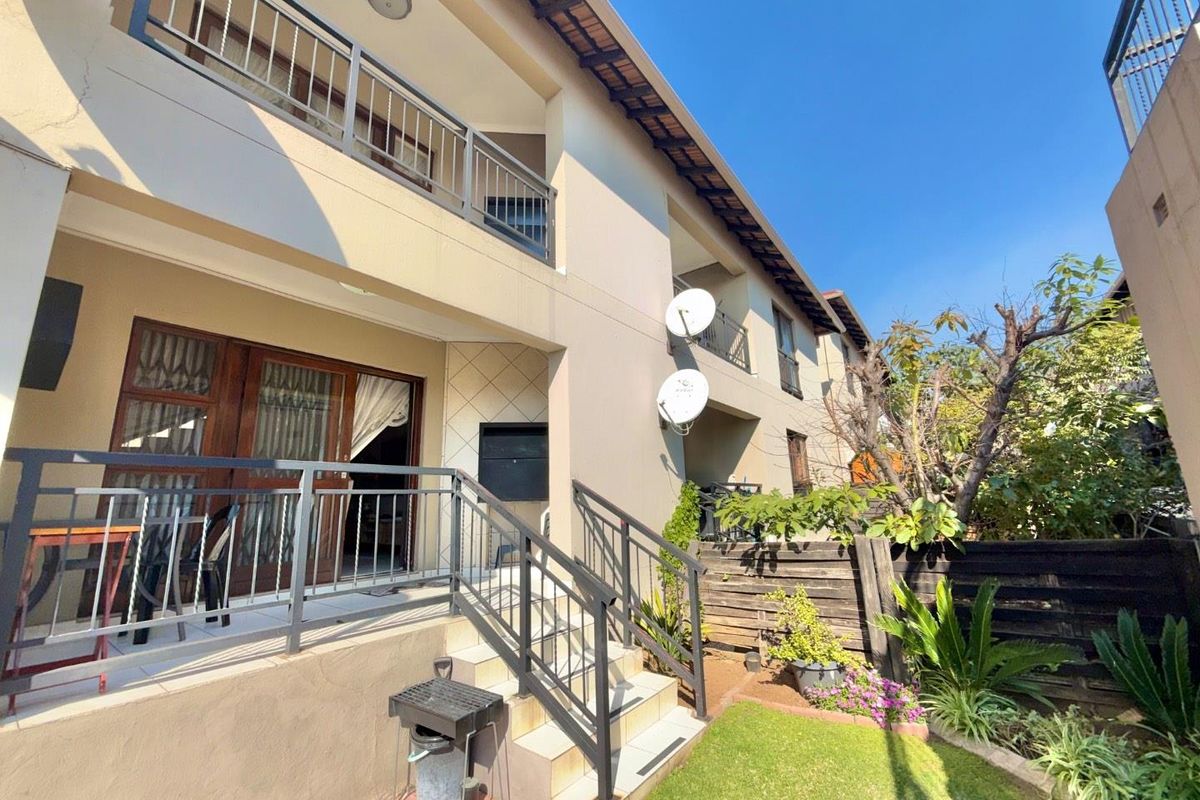 Rear exterior view of the townhouse featuring a private patio, built-in braai, metal balcony railings, and a small landscaped garden area.