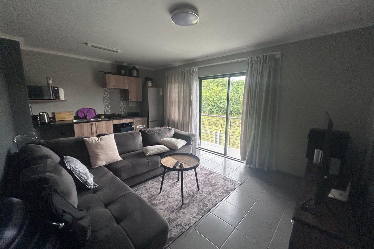 Open-plan living area featuring a compact kitchen with built-in cabinetry and tiled flooring, leading to a sliding glass door with access to a balcony.