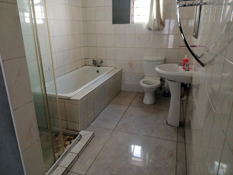 A functional bathroom featuring a bathtub, separate shower enclosure, pedestal basin, and toilet with neutral wall and floor tiling.