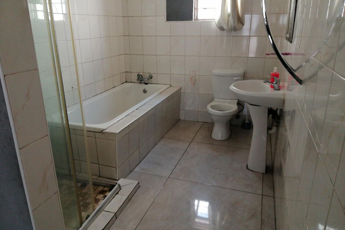 A functional bathroom featuring a bathtub, separate shower enclosure, pedestal basin, and toilet with neutral wall and floor tiling.