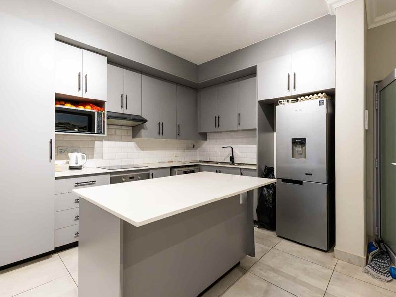 Modern kitchen featuring grey cabinetry, a central island with quartz countertops, subway tile backsplash, and integrated appliances.