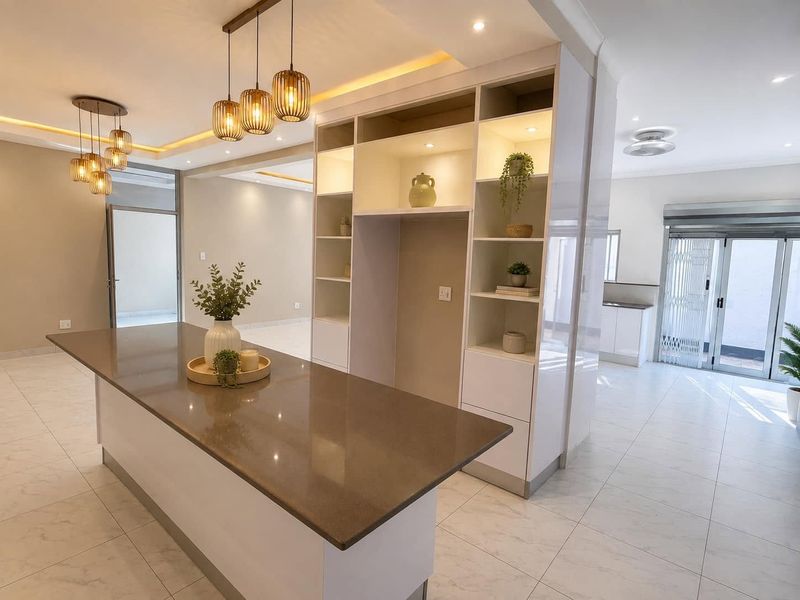 Modern open-plan living area featuring a central kitchen island with stone countertops, built-in display shelving, and bright, neutral tiled flooring throughout.