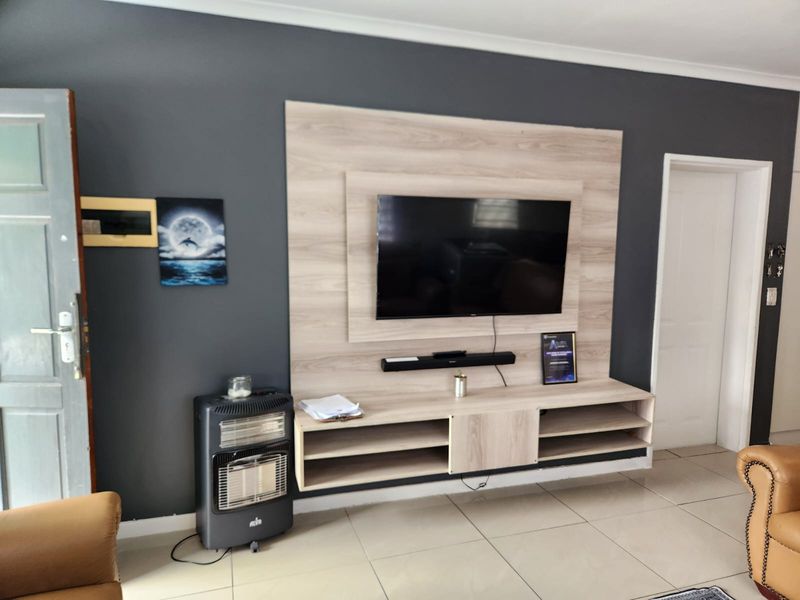 Living room featuring a modern built-in media unit with light wood-grain finish, dark accent wall, and neutral tiled flooring.