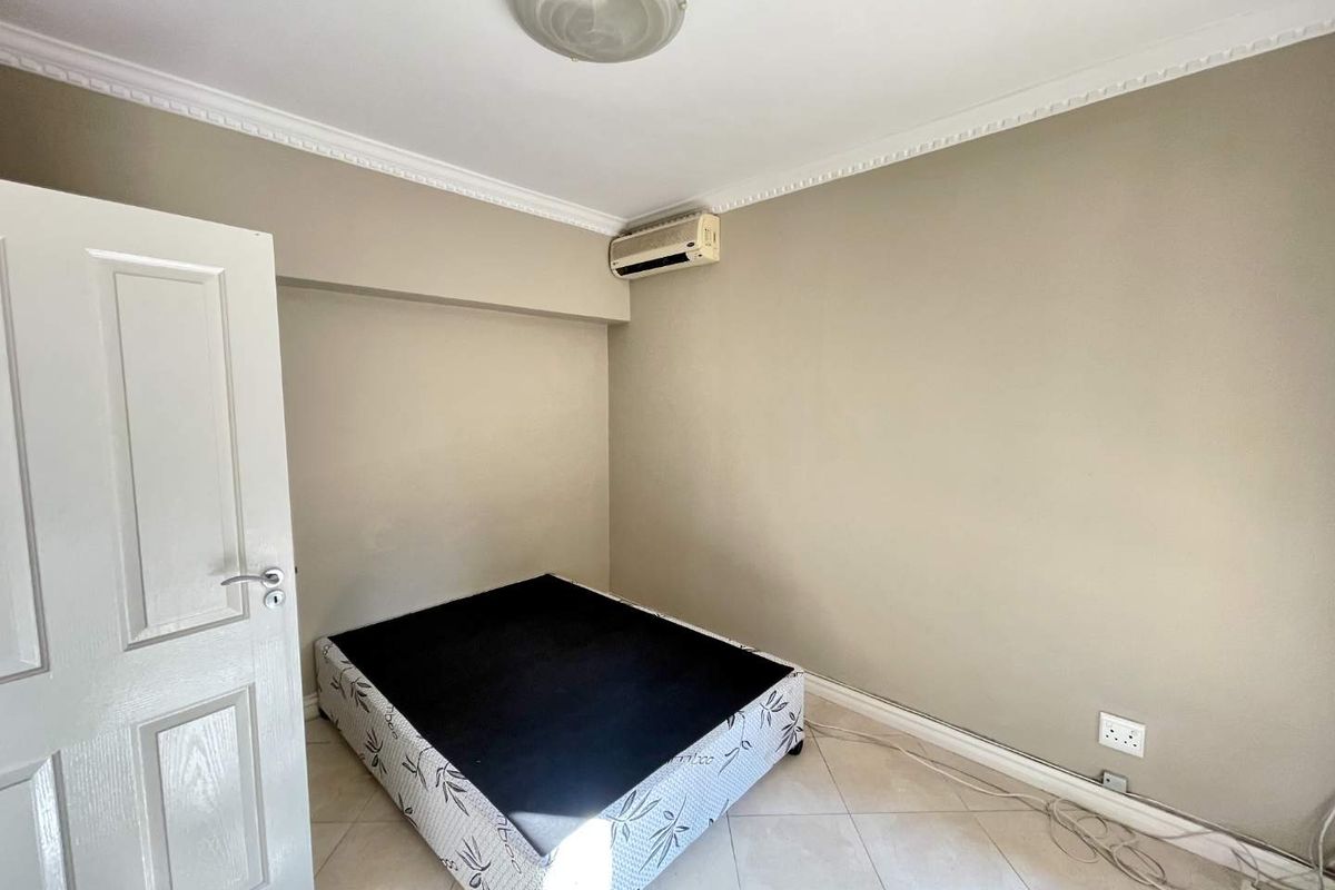 A bedroom featuring tiled flooring, crown molding, and a wall-mounted air conditioning unit.