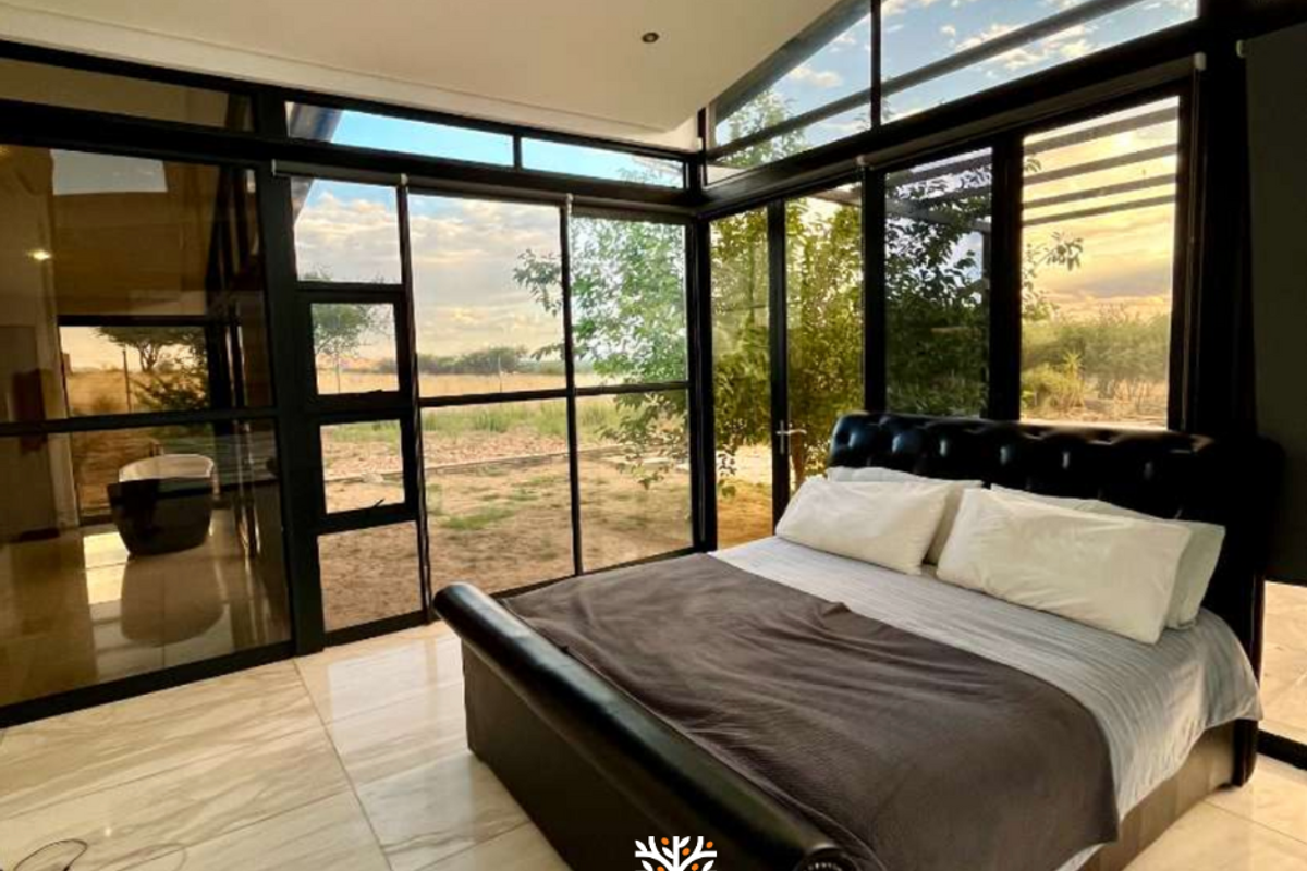 Modern bedroom featuring expansive floor-to-ceiling glass walls, sleek tiled flooring, and an integrated en-suite bathroom area with a contemporary freestanding bathtub.