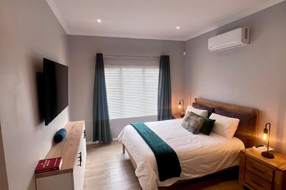 A well-maintained bedroom featuring tiled flooring, recessed downlighting, and a wall-mounted split-system air conditioner.