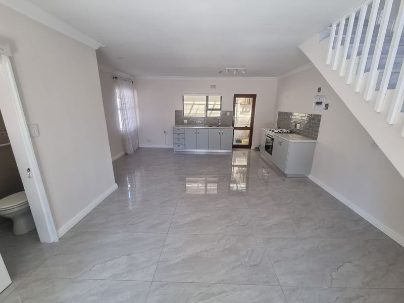 An open-plan living and kitchen area featuring modern grey cabinetry, a gas hob, oven, and polished tiled flooring, with an adjacent staircase.