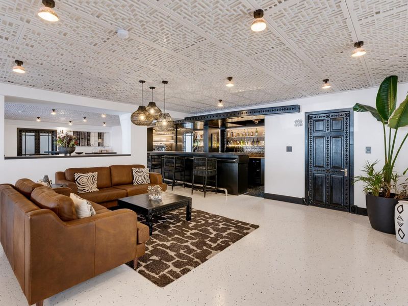 A sophisticated bar area featuring a built-in counter, decorative ceiling panels, recessed lighting, and a distinctive ornate wooden door.