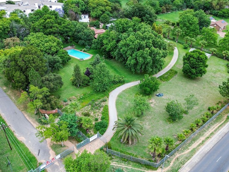 Aerial view of a spacious farm property featuring a swimming pool, extensive landscaped gardens, mature trees, and a paved driveway with gated access.