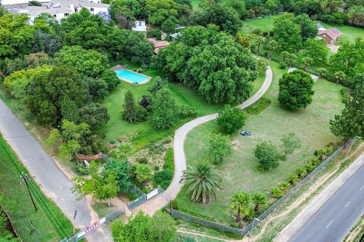 Aerial view of a spacious farm property featuring a swimming pool, extensive landscaped gardens, mature trees, and a paved driveway with gated access.