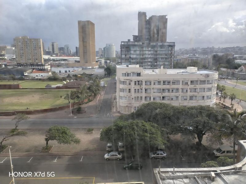 An elevated urban view overlooking surrounding city buildings, streets, and green spaces from an apartment window.