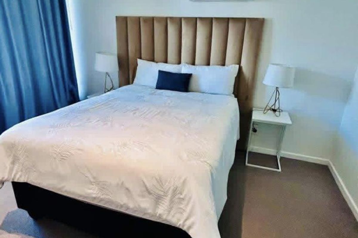 A well-maintained bedroom featuring neutral carpet flooring, a wall-mounted split-system air conditioner, and horizontal venetian blinds for privacy.