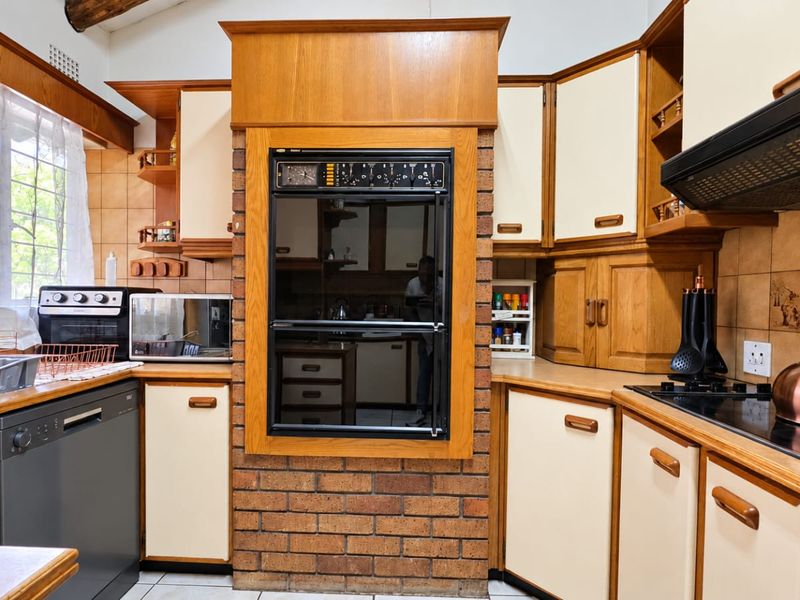 A traditional kitchen featuring wooden cabinetry, a built-in oven set into a brick feature wall, and tiled backsplash with ample counter space.