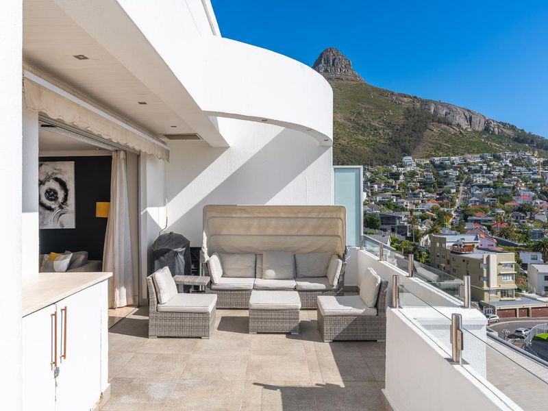 Spacious balcony featuring a glass balustrade, tiled flooring, and built-in cabinetry, offering stunning mountain and urban views.