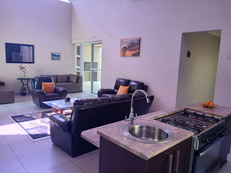 Spacious open-plan living area featuring a kitchen island with a gas hob, sink, and direct access to an outdoor patio through sliding glass doors.