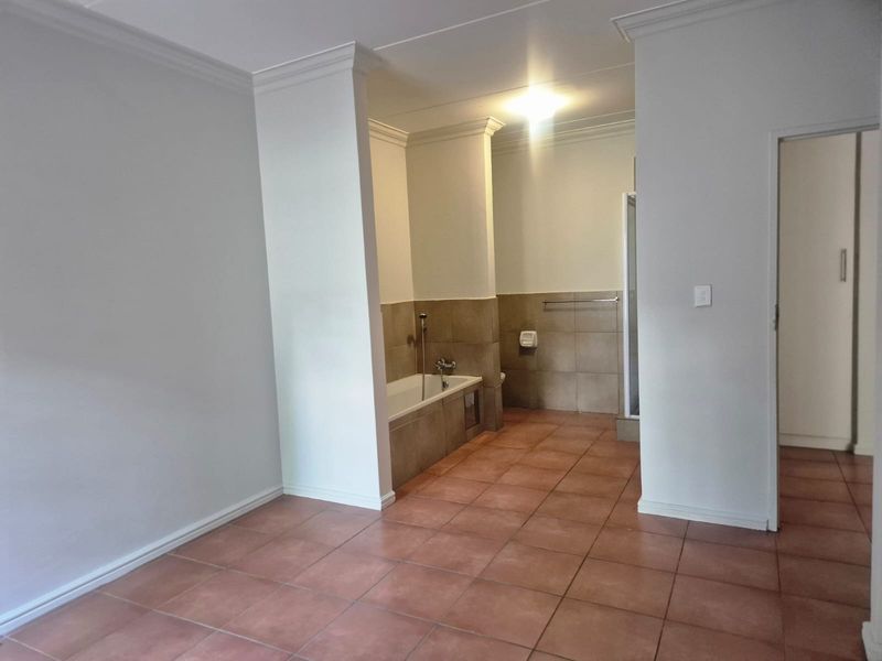 An open-plan bathroom featuring a built-in bathtub, separate shower enclosure, and neutral ceramic floor and wall tiling.