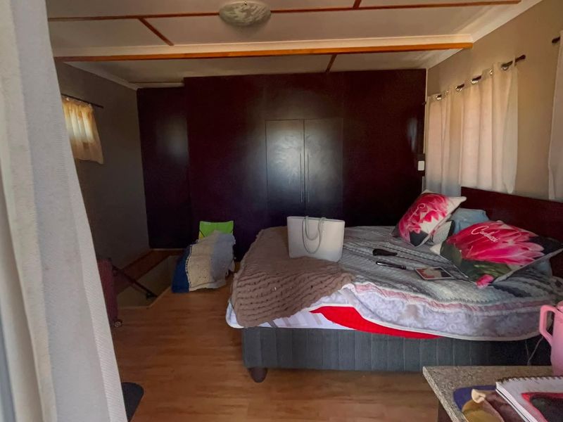 A bedroom featuring laminate flooring, exposed ceiling beams, and a dark built-in wardrobe.