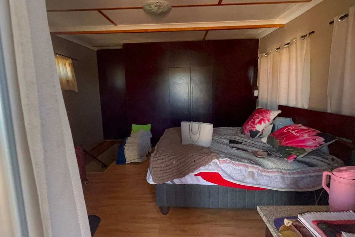 A bedroom featuring laminate flooring, exposed ceiling beams, and a dark built-in wardrobe.