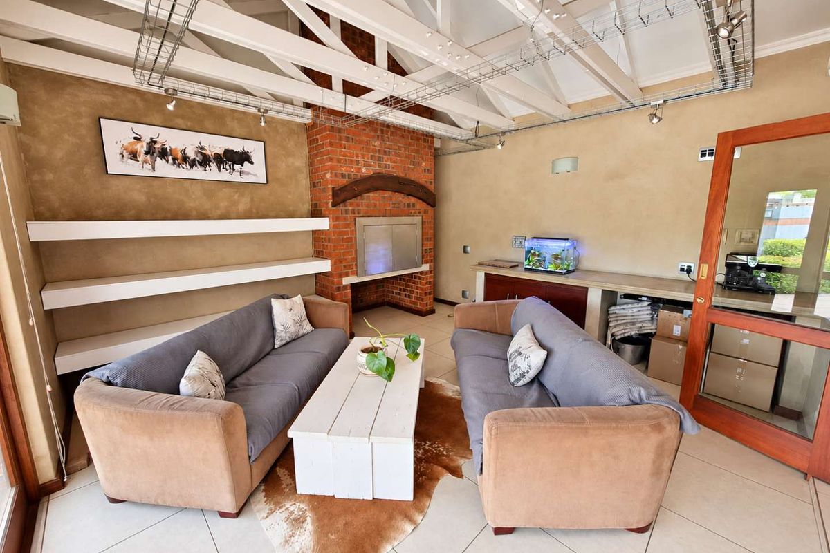 Spacious living area featuring exposed white roof trusses, a prominent brick fireplace, built-in shelving, and neutral tiled flooring.