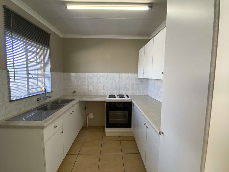 A functional galley-style kitchen featuring white cabinetry, laminate countertops, a built-in electric oven and hob, and tiled flooring.