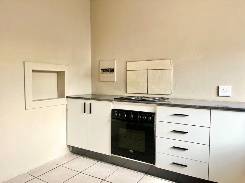 A compact kitchen featuring white cabinetry, a built-in oven with electric hob, and tiled flooring, ready for a modern update.