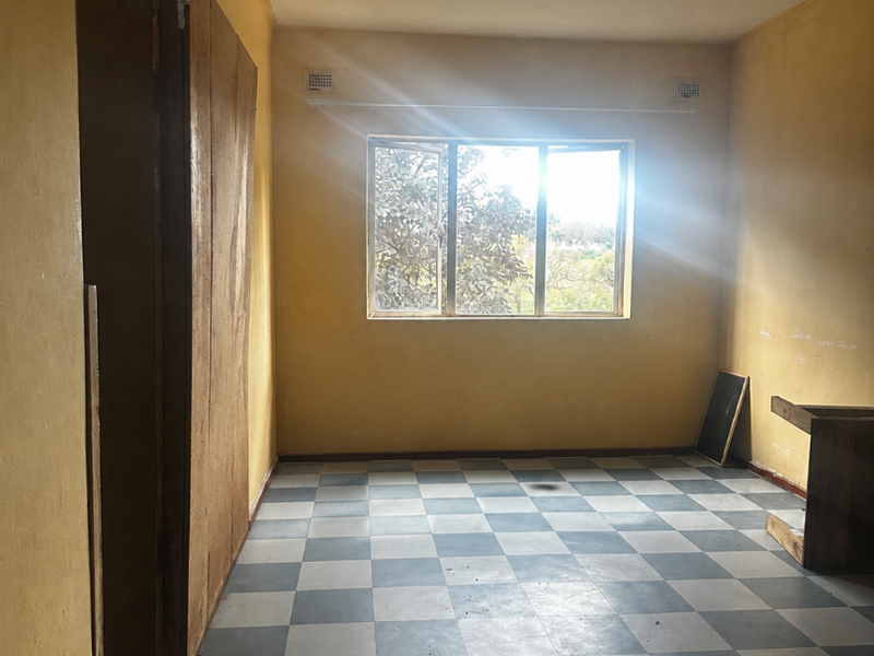 An empty bedroom featuring checkered vinyl flooring, built-in cupboards, and yellow walls, requiring renovation to update the dated finishes.