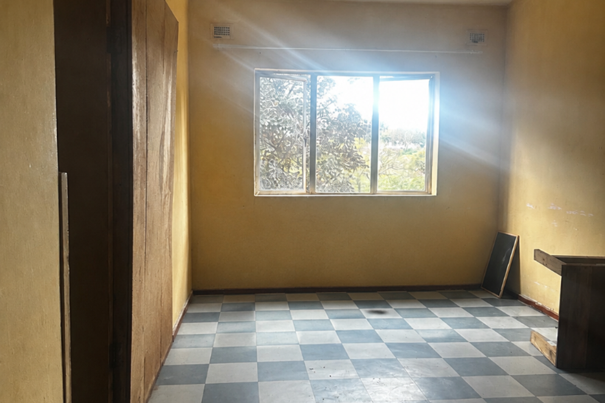 An empty bedroom featuring checkered vinyl flooring, built-in cupboards, and yellow walls, requiring renovation to update the dated finishes.